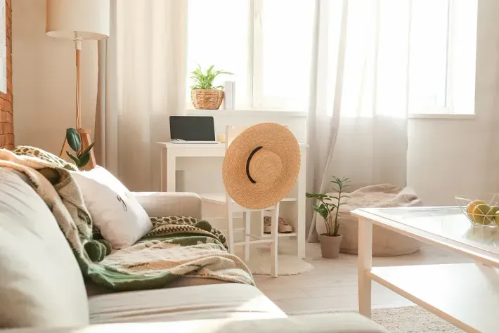 Acogedora sala de estar con sofá, sombrero de paja en un taburete y ventana soleada.