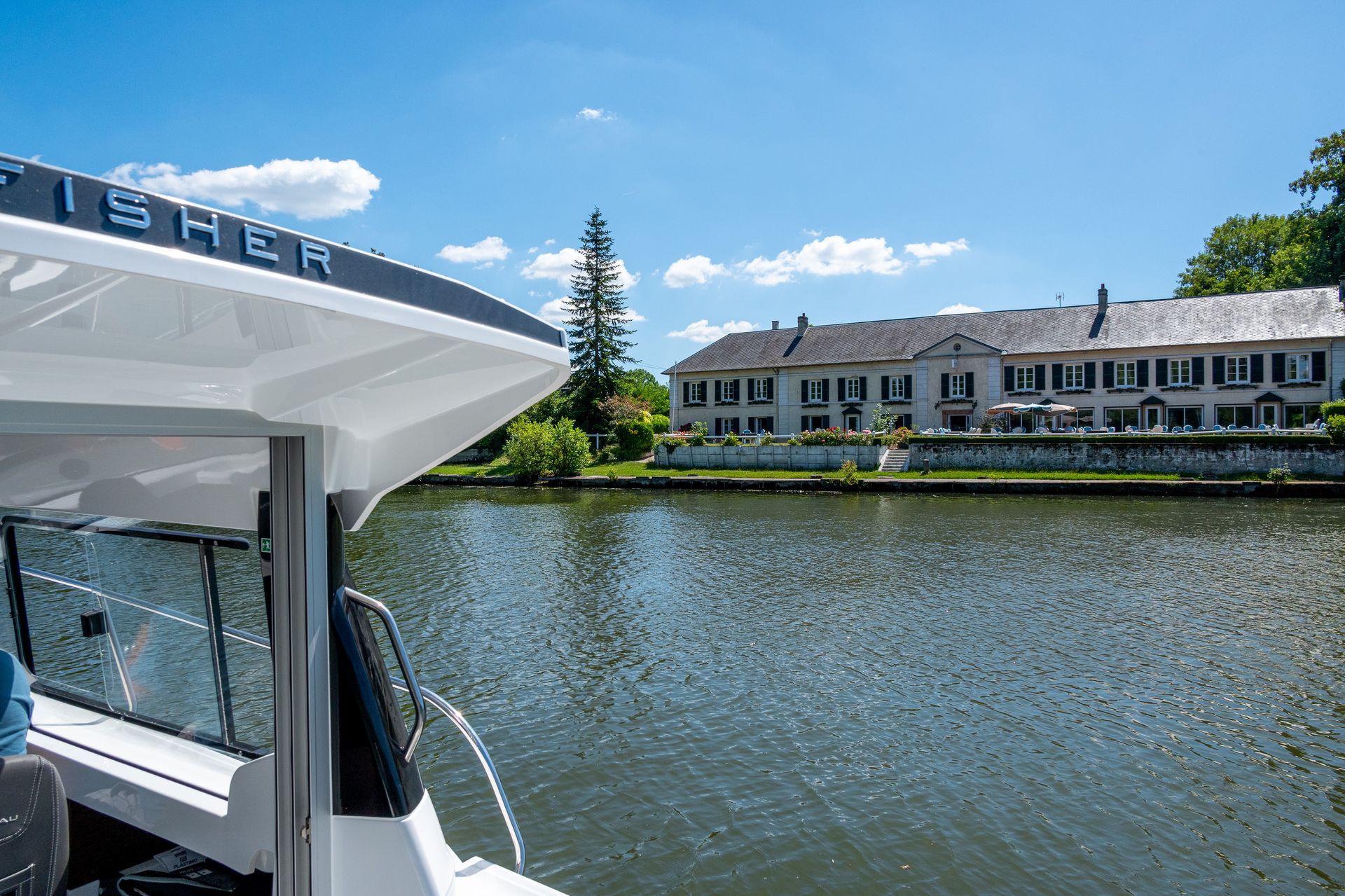 Bateau naviguant sur l'eau près d'un grand bâtiment avec des arbres et un ciel bleu.
