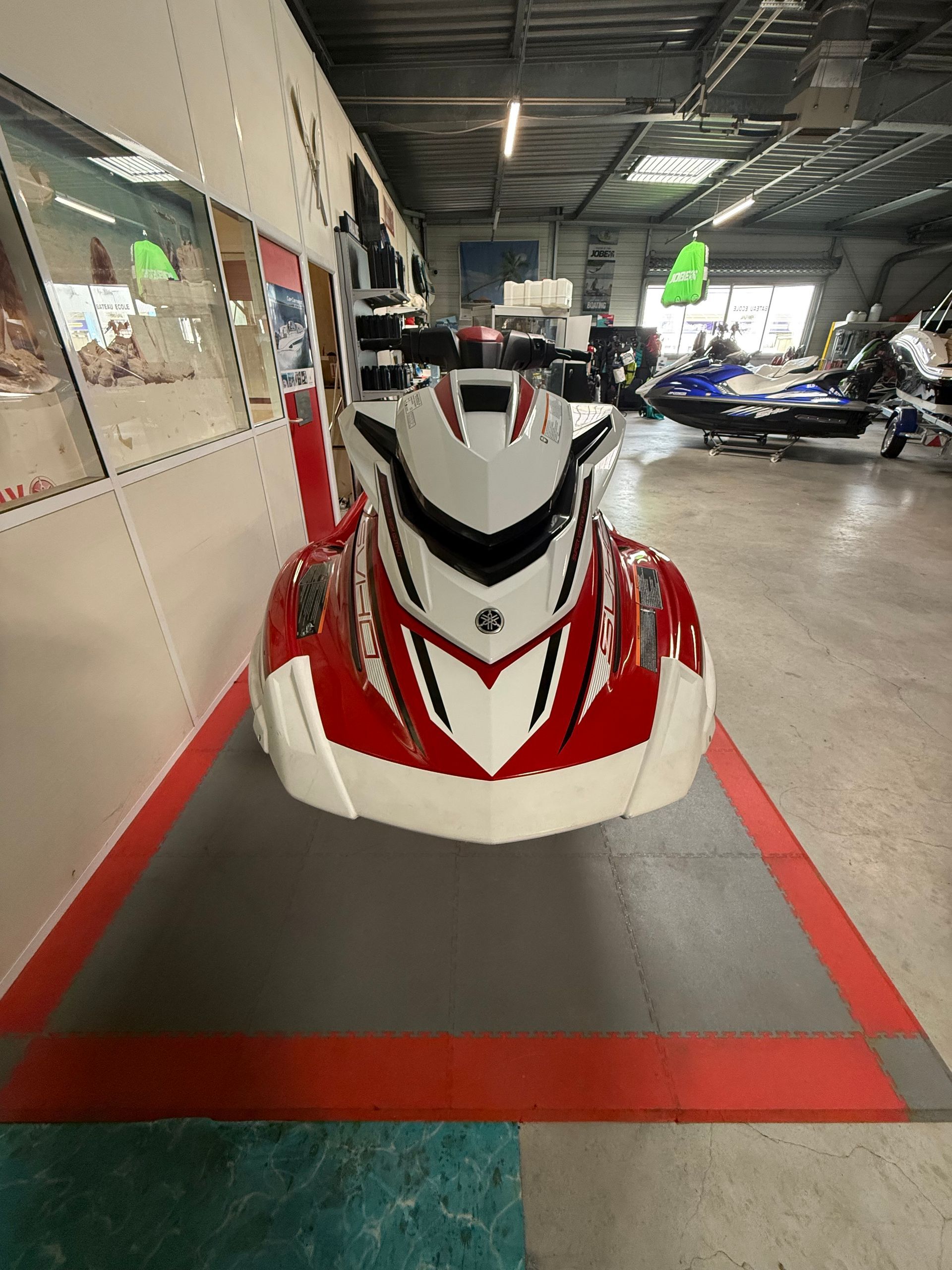 Jet ski rouge et blanc sur un tapis gris et rouge à l'intérieur d'un garage.