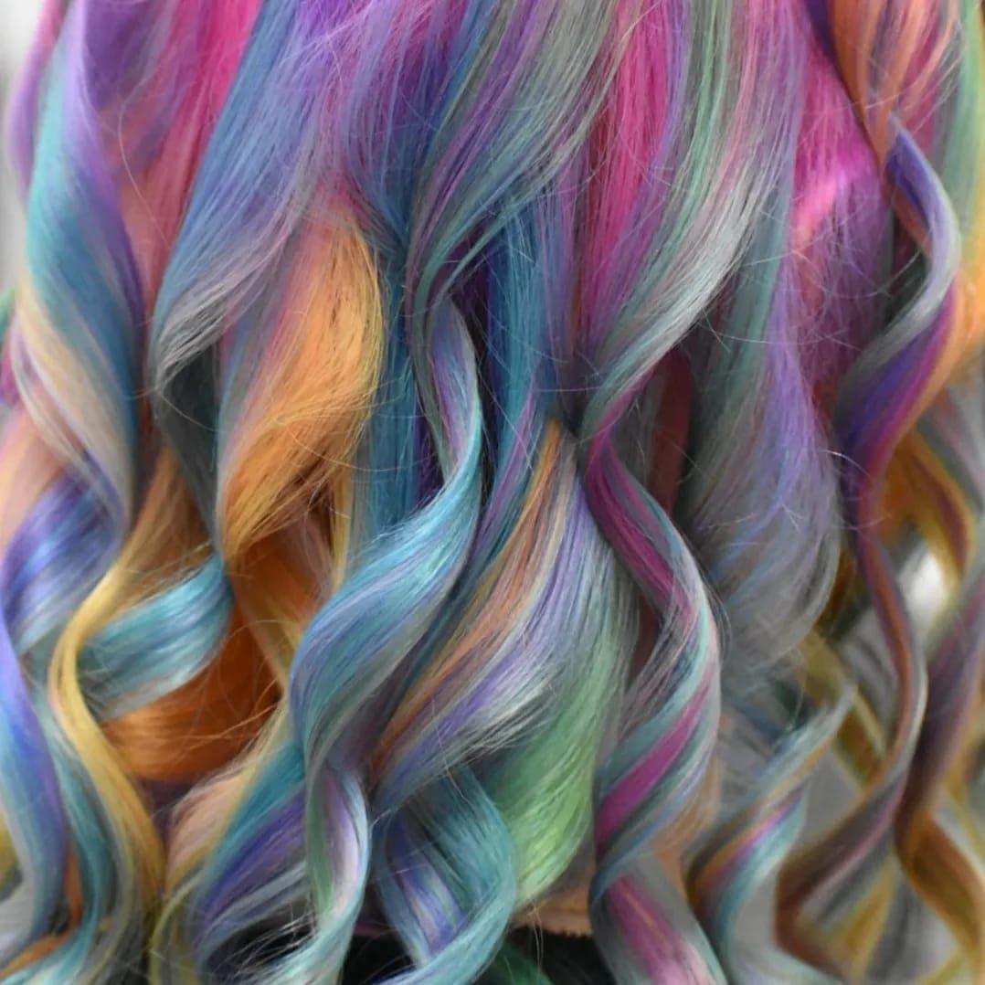Primer plano de cabello ondulado de colores arcoíris con mechones rosas, azules, amarillos y morados.
