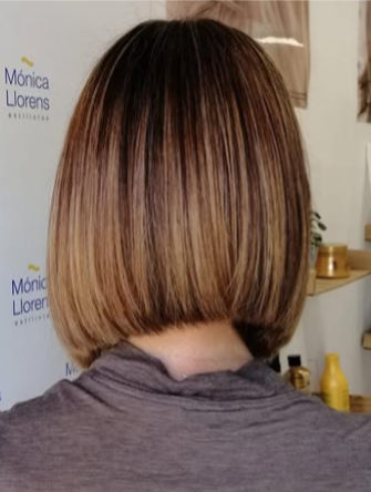 Corte de pelo bob rubio con raíces oscuras y camisa marrón que deja ver el logotipo del salón.