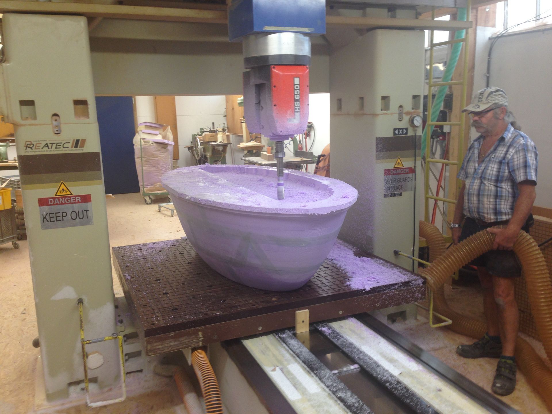 A man is standing next to a machine that is cutting a purple bowl.