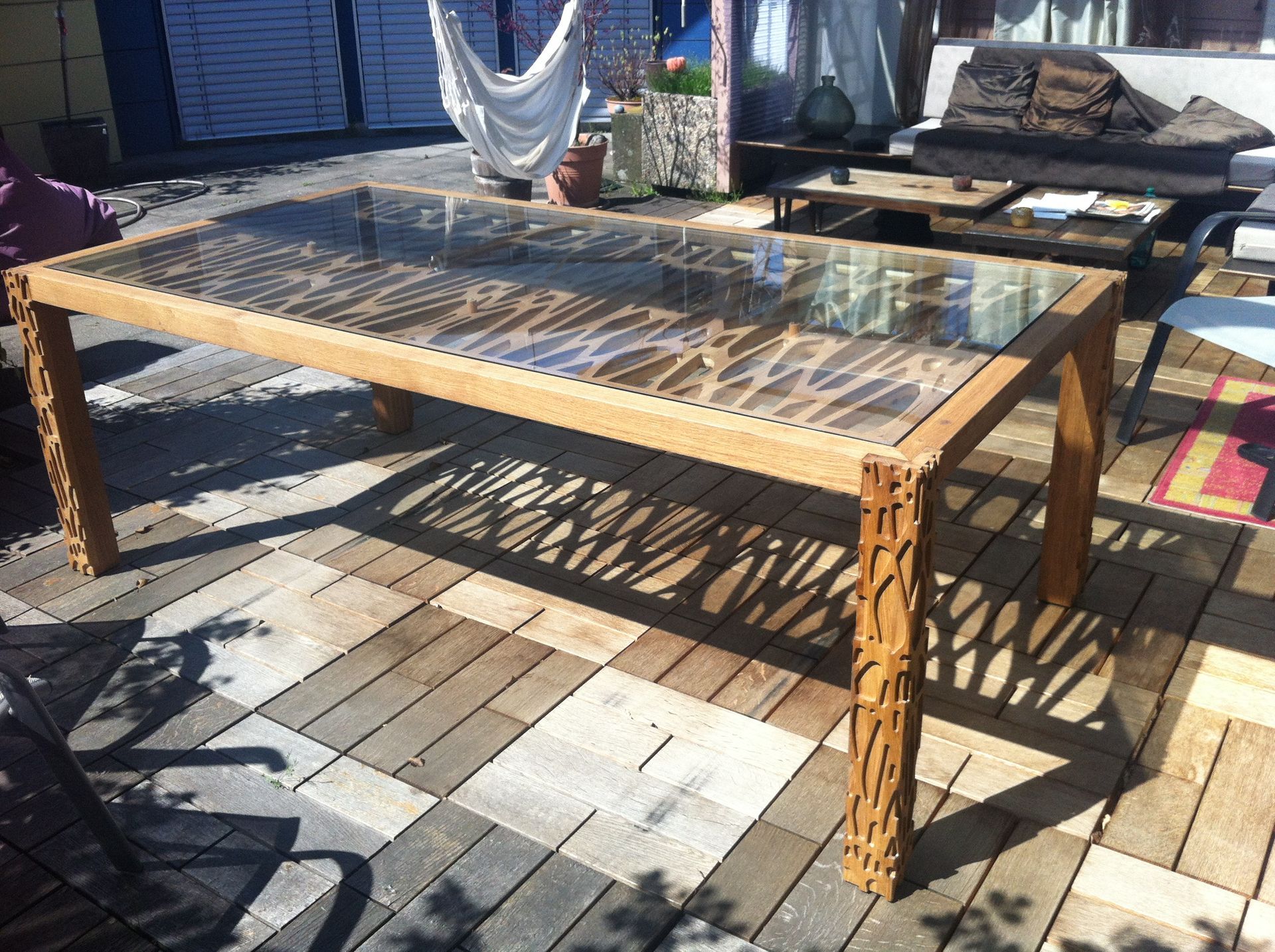 A wooden table with a glass top is sitting on a patio.