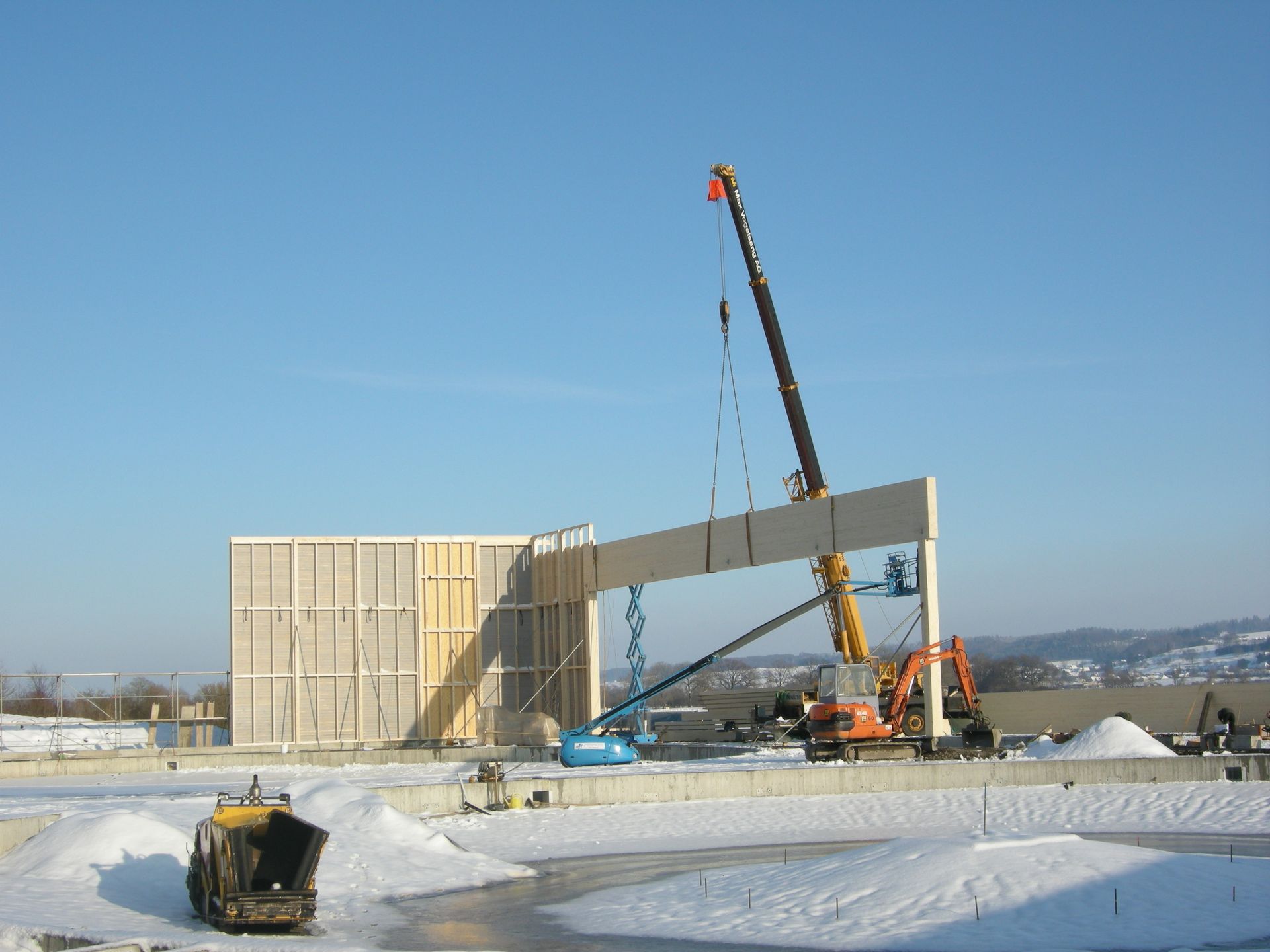 A crane is lifting a large piece of wood in the snow