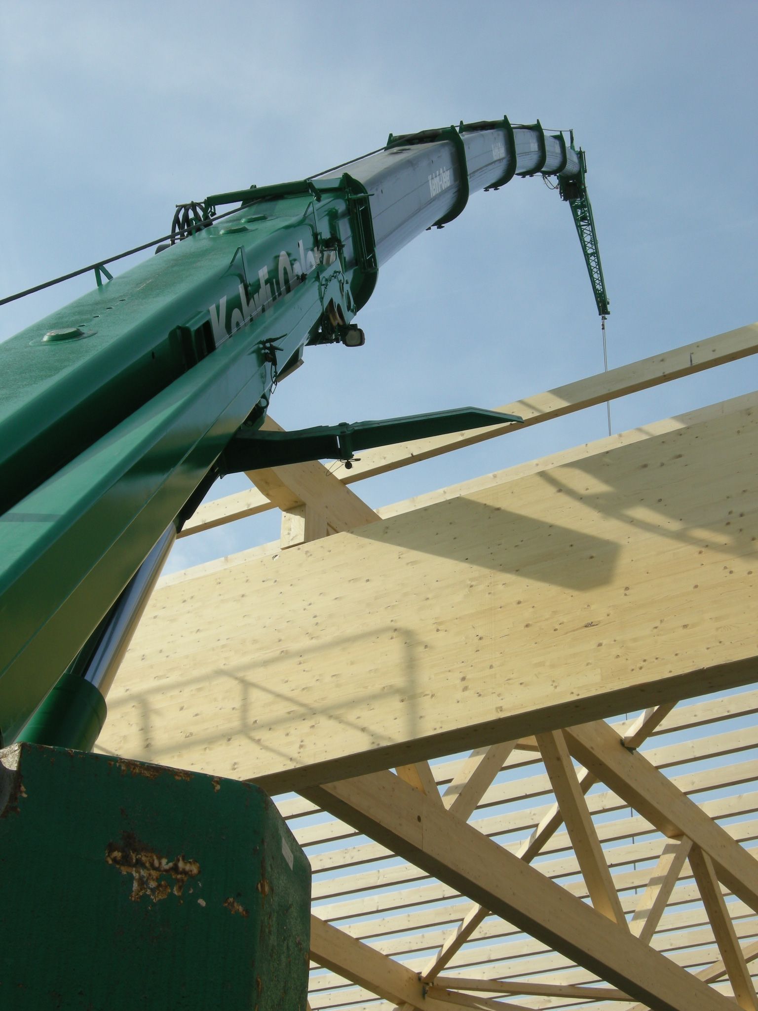 A large green crane is lifting a wooden structure