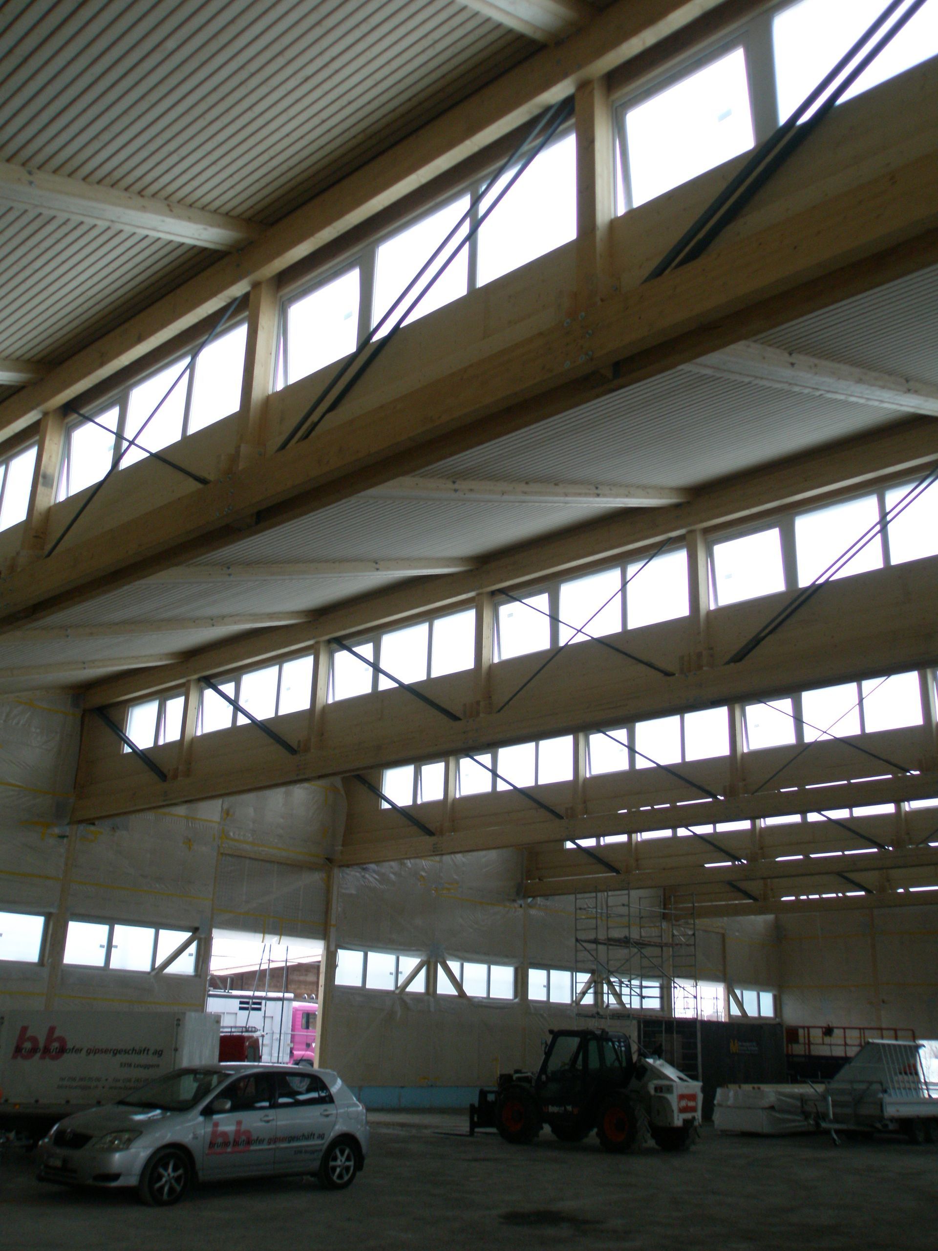 A white car is parked in a large building with lots of windows