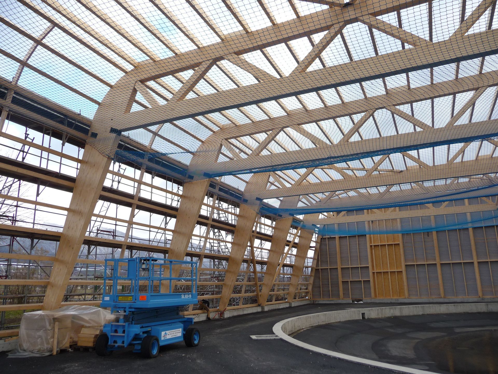 A blue aerial lift is parked in front of a building under construction.