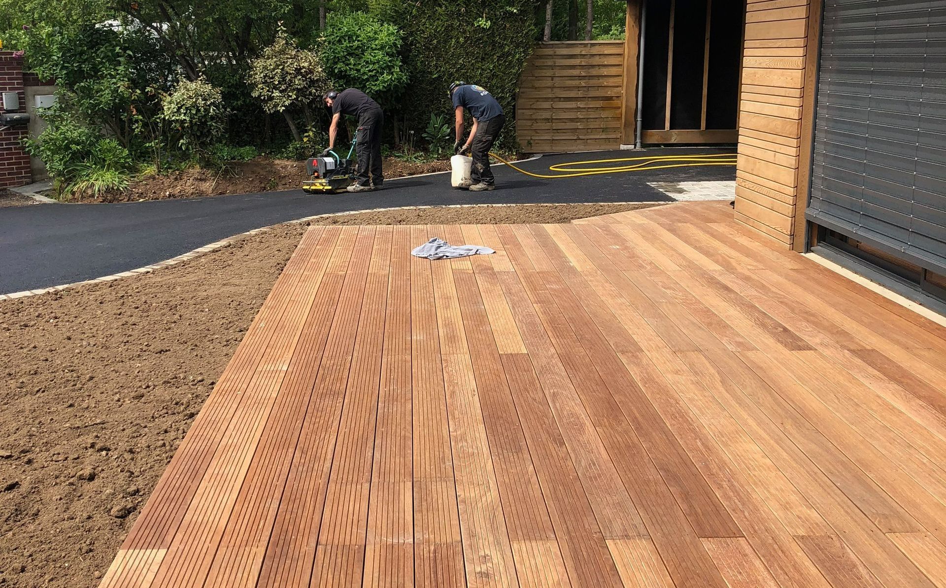Terrasse en bois et deux ouvriers qui goudronnent une allée