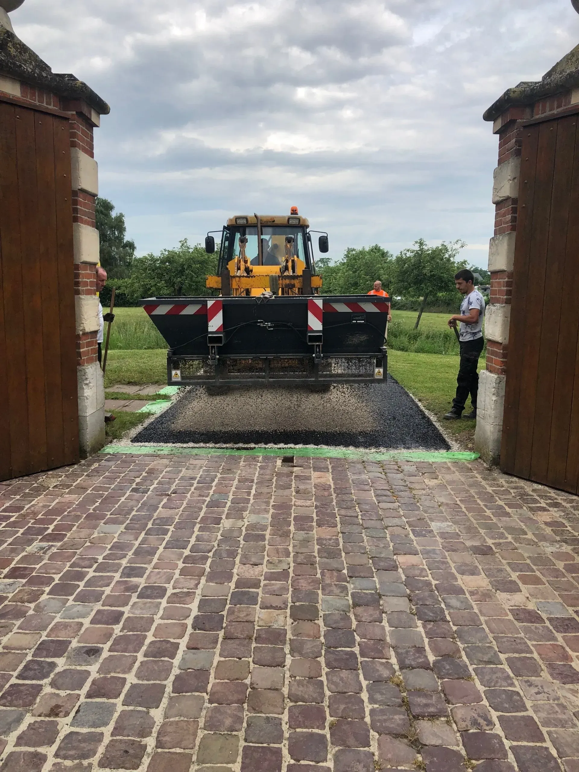 Une machine réalise le bétonnage d'une allée à côté d'un portail ouvert