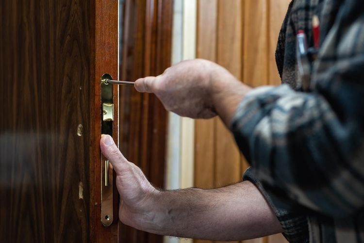 Manos instalando una manija de latón en una puerta de madera.