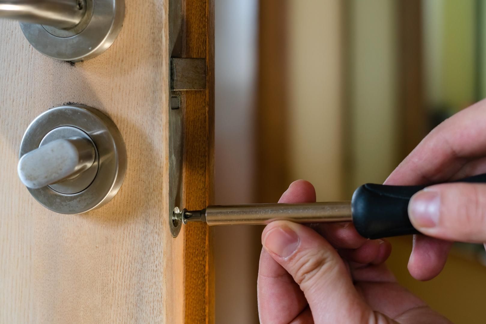 Mano usando un destornillador para ajustar la cerradura de una puerta de madera.