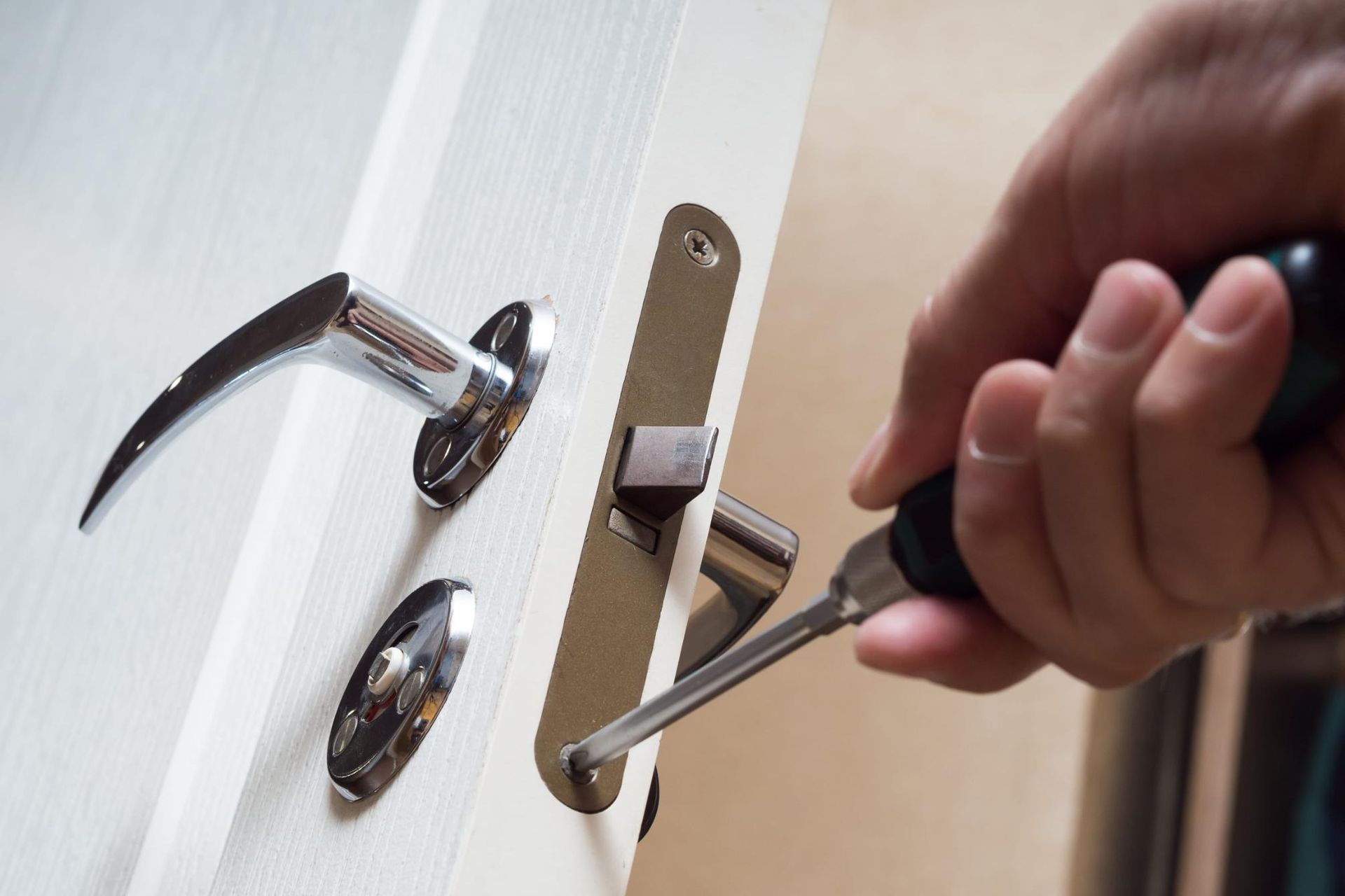 Mano usando un destornillador para instalar una manija de puerta en una puerta blanca