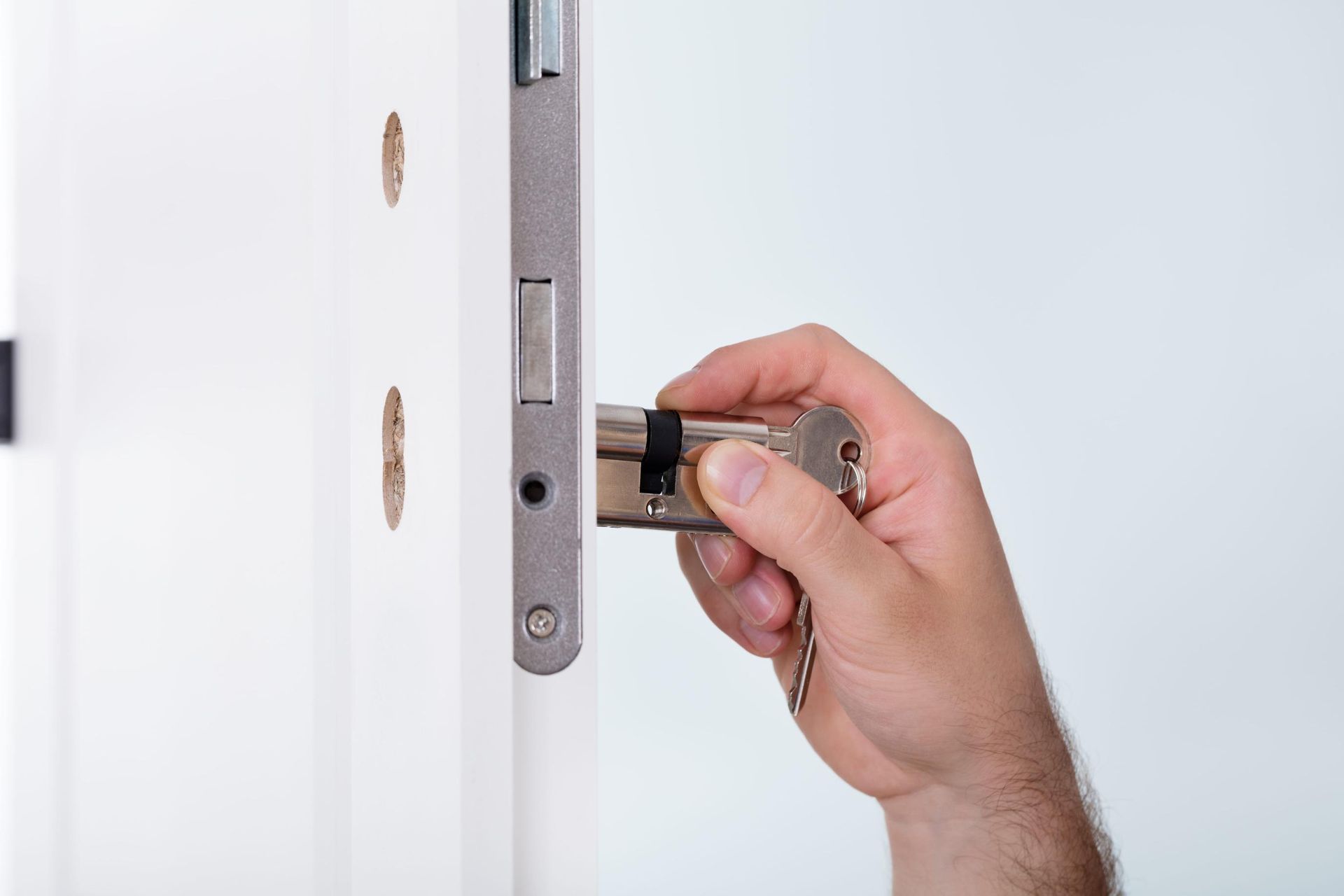 Una mano sostiene una llave en la cerradura de una puerta blanca.