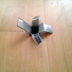 Metallobjekt mit vier gebogenen Klingen, zentriert auf einem Holzboden.