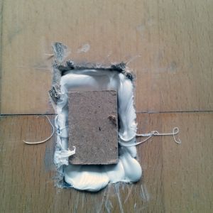Holzboden mit einem rechteckigen Reparaturflicken, der mit weißer Dichtungsmasse befestigt ist.