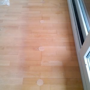 Heller Holzboden mit drei kreisförmigen, hellen Flecken in der Nähe einer Glasschiebetür.