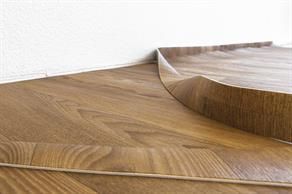 Holzoptik-Bodenbelag, der sich in der Nähe einer weißen Wand aufwölbt.