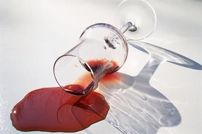 Verschütteter Rotwein auf einer weißen Oberfläche mit einem umgestürzten Glas. Sonnenlicht wirft einen Schatten.