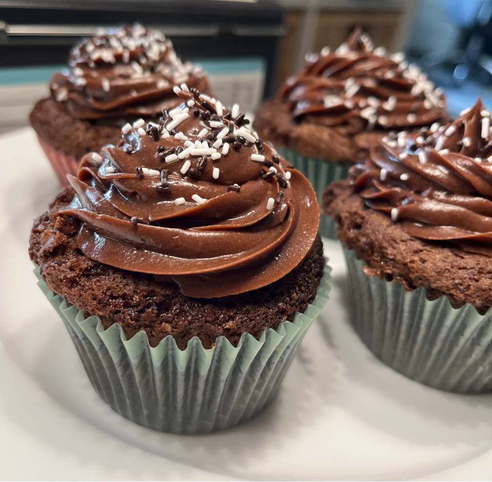 Schokoladen-Cupcakes mit spiralförmigem Zuckerguss und Streuseln auf einem weissen Teller