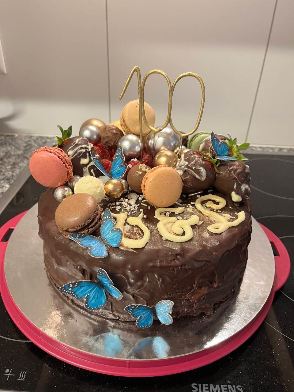 Dekorierter Schokoladenkuchen mit goldenen und blauen Akzenten und bunten Macarons als Topping