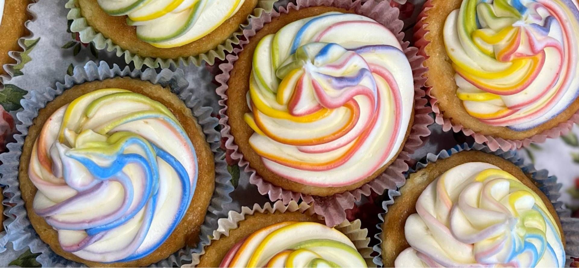 Bunte, mit Zuckerguss überzogene Cupcakes mit spiralförmigem Zuckerguss, Rosa, Gelb und Weiss, dicht beieinander angeordnet