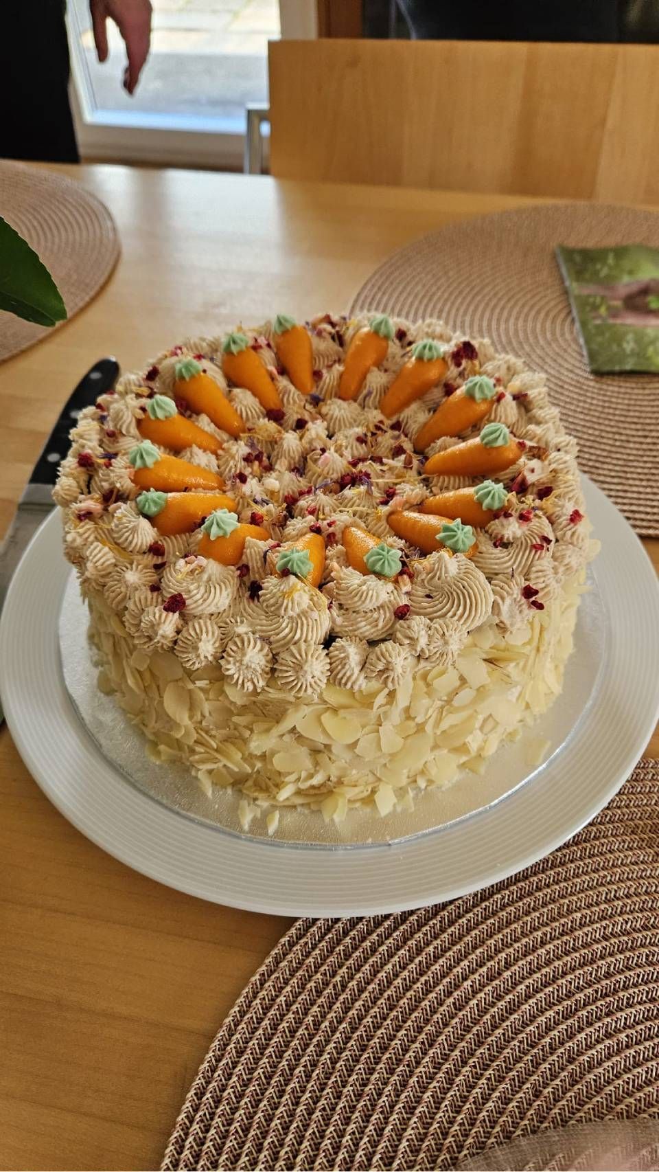 Ein runder, mit Orangenscheiben und Streuseln verzierter Kuchen auf einem weissen Teller auf einem Holztisch.
