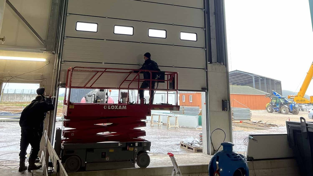 Ouvriers qui installent une porte d'entrepôt à l'aide d'une nacelle rouge