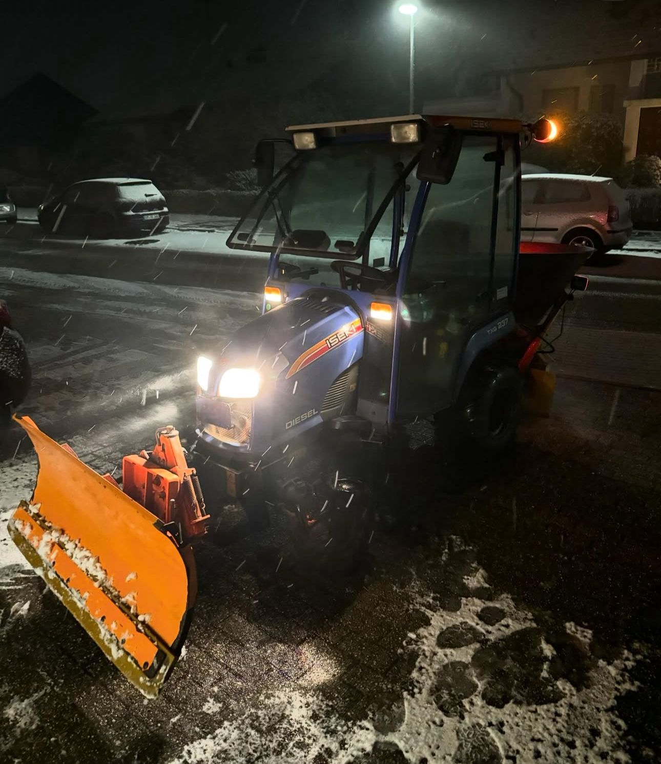 Ein blau-oranger Traktor mit einem daran befestigten Schneepflug