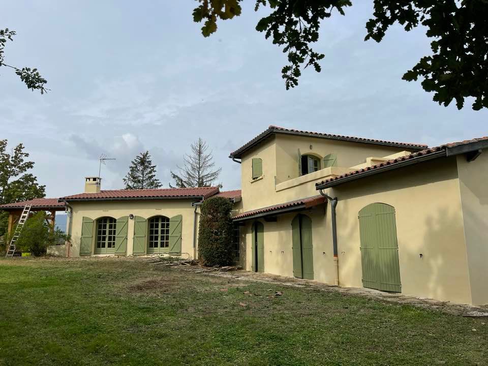 Façade d'une maison jaune aux volets vert