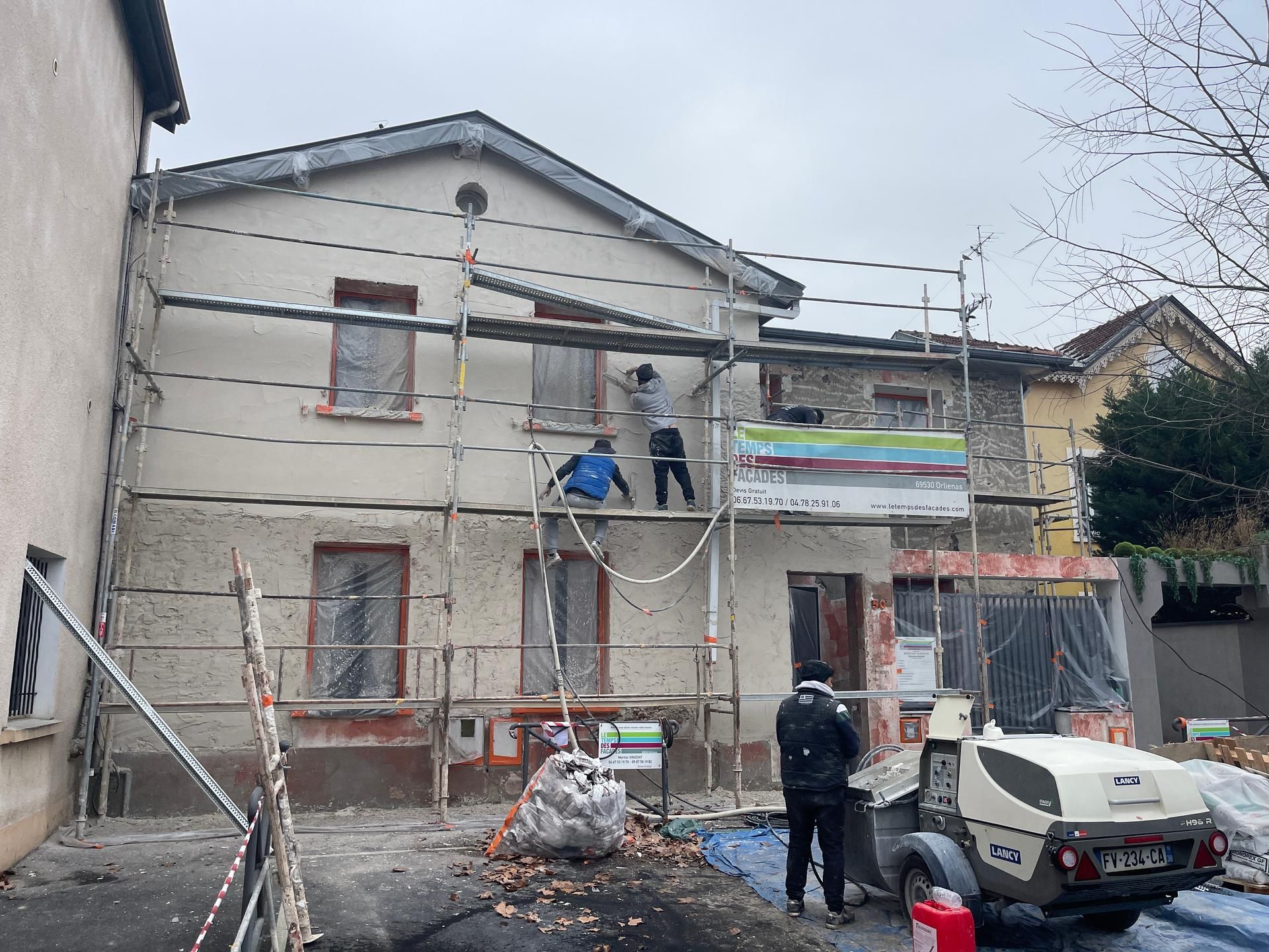 Équipe de façadiers sur échafaudage en train de talocher de l'enduit