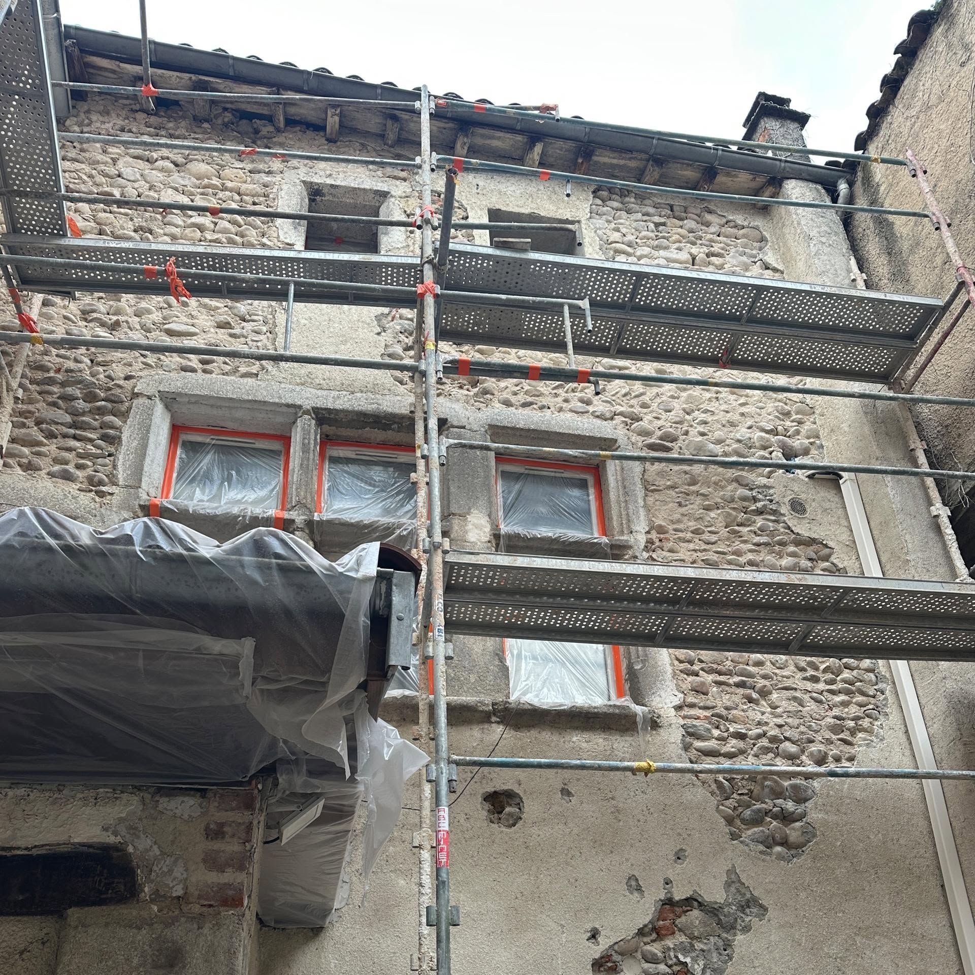 Façade en pisé et pierre avec échafaudage