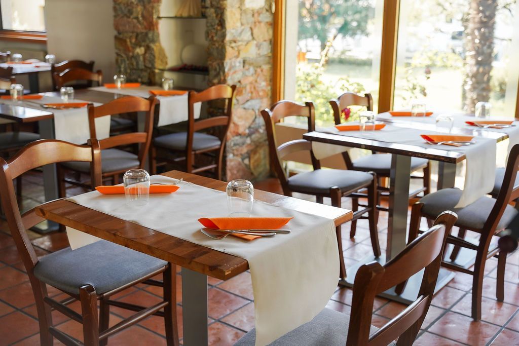 Accogliente sala da pranzo del ristorante con tavoli in legno, tovaglie bianche, tovaglioli arancioni e pareti in pietra.