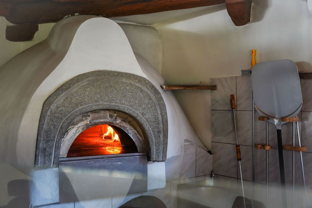 Un forno in pietra con il fuoco acceso in una cucina rustica, con utensili e attrezzi appesi accanto.