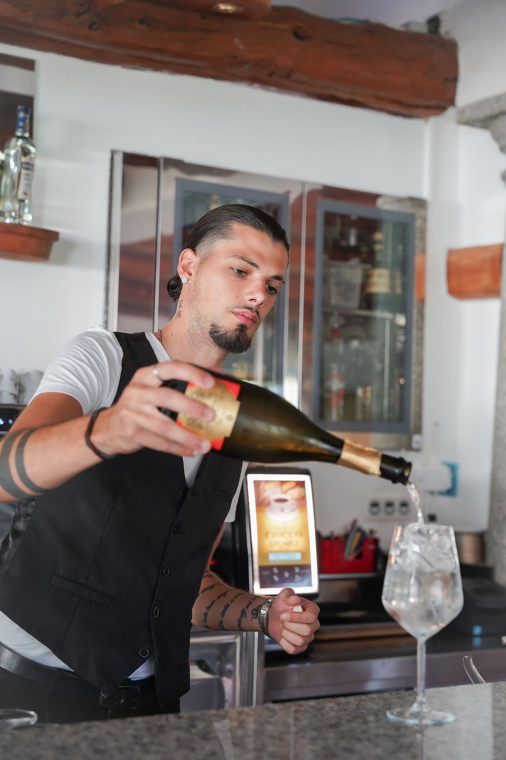Un barista versa una bevanda da una bottiglia in un bicchiere dietro al bancone.