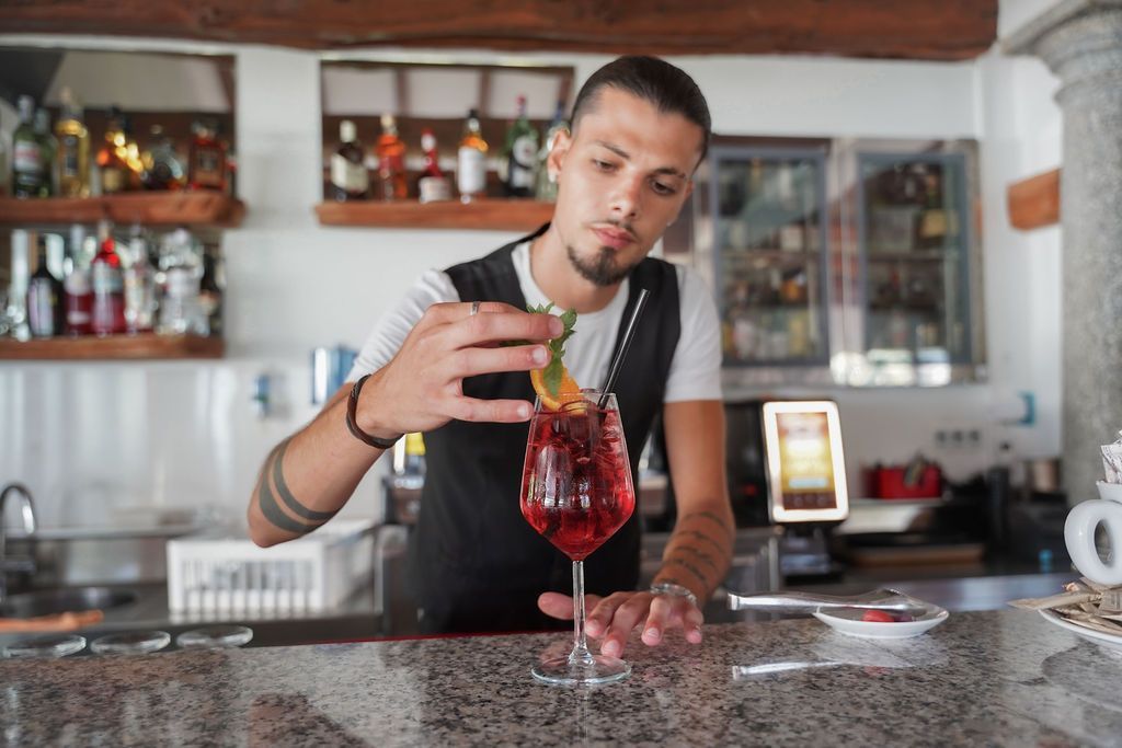 Un barista versa un cocktail rosso da uno shaker in un bicchiere con stelo al bancone di un bar.