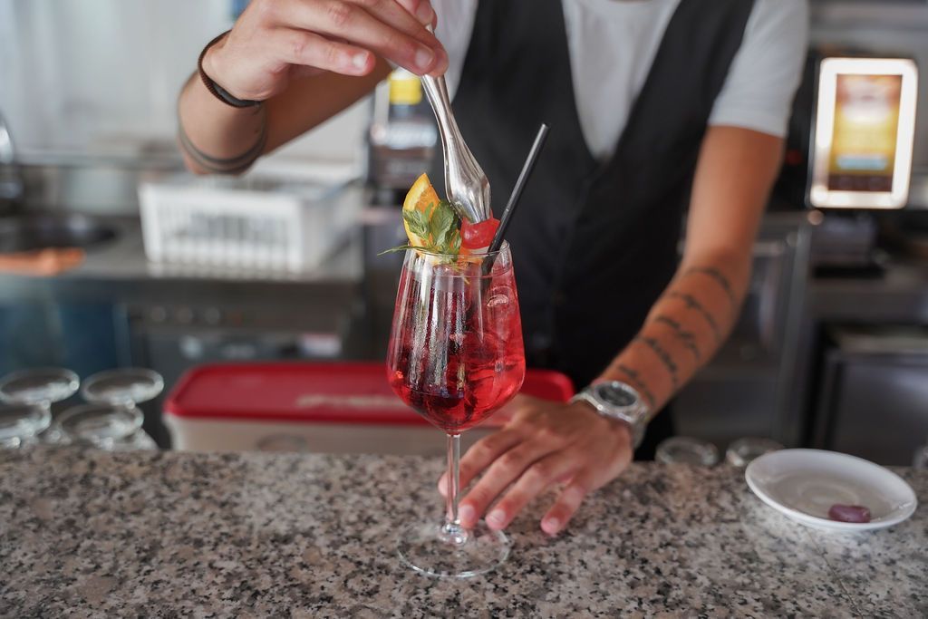 Un barista versa un cocktail rosso in un bicchiere con stelo su un bancone di granito.