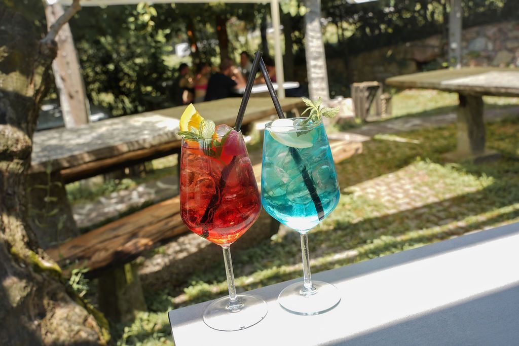 Due cocktail colorati con guarnizione di frutta su un tavolo all'aperto in un giardino soleggiato.