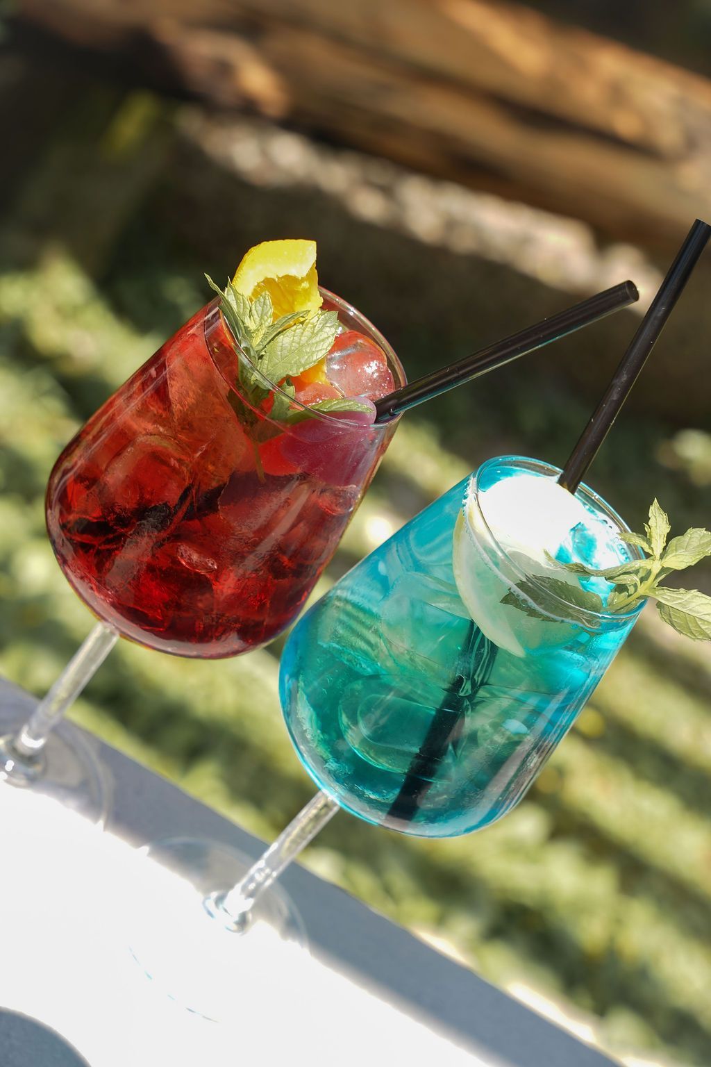 Due cocktail colorati con cannucce e guarnizione di agrumi su un tavolo all'aperto illuminato dal sole.