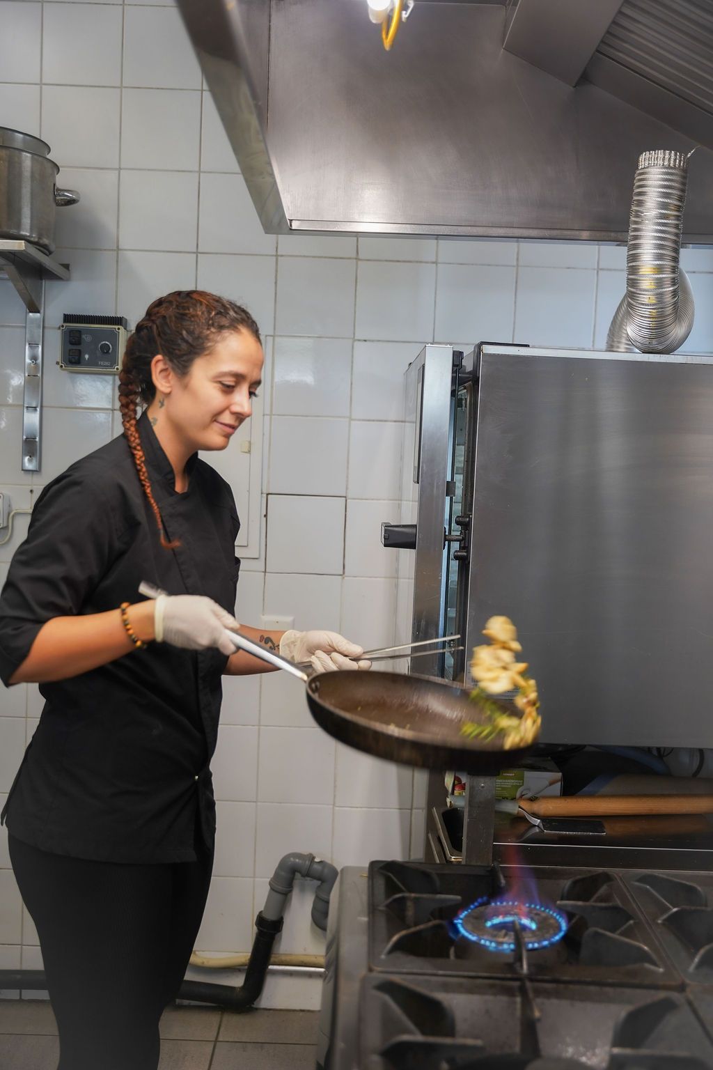 Uno chef che salta il cibo in un wok su una fiamma a gas blu in una cucina professionale.