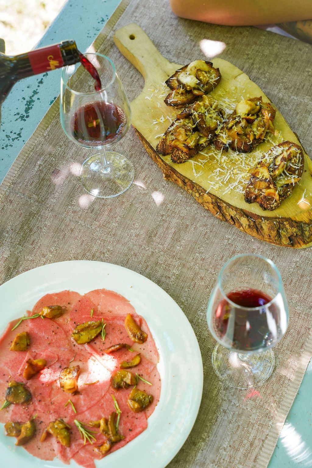 Due brindisi aperti e due bicchieri di vino rosso su un tavolo illuminato dal sole.