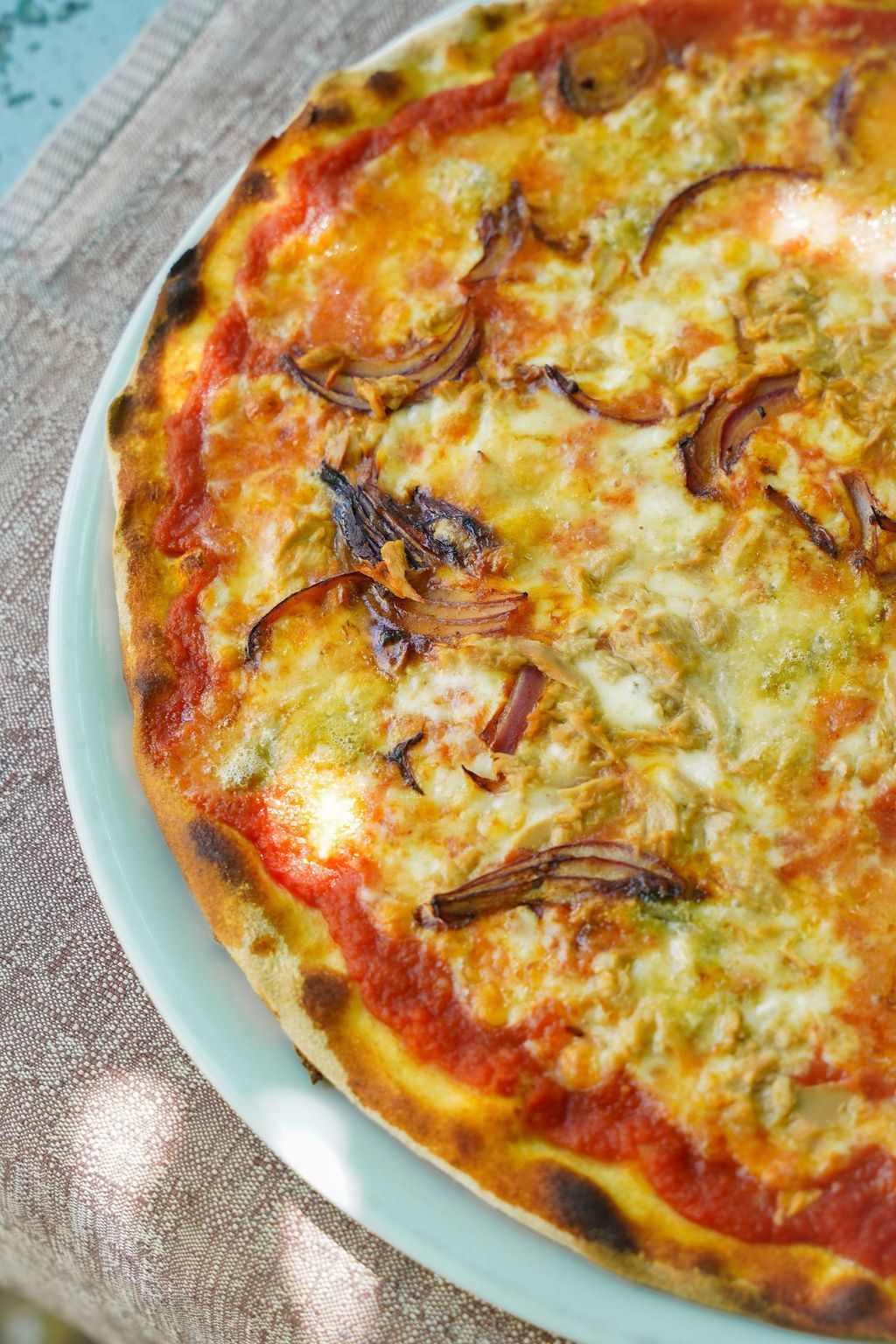 Primo piano di una pizza alle cipolle dorata su un piatto, con una crosta croccante e formaggio fuso.