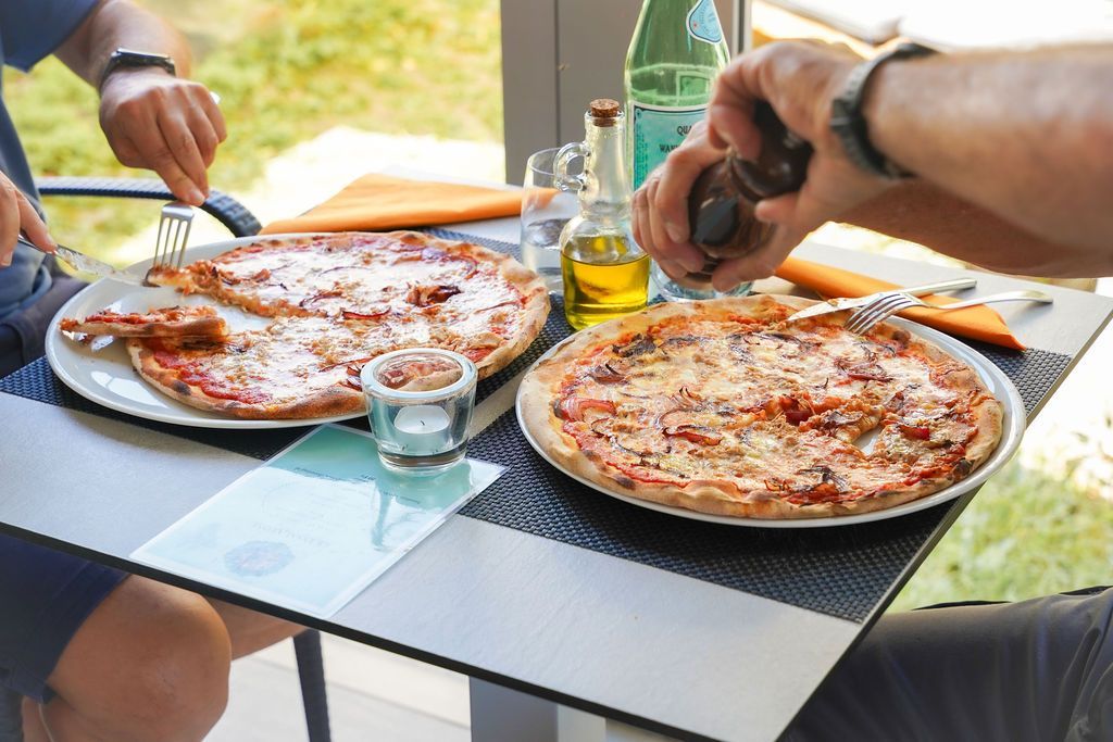 Persone che servono la pizza all'aperto a un tavolo con bevande e olio d'oliva