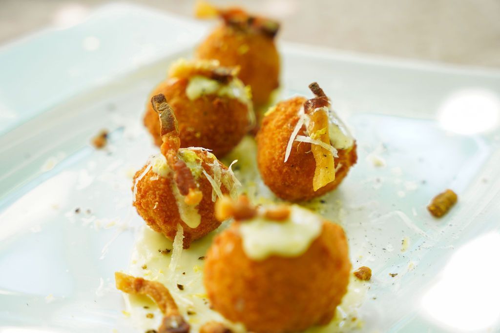 Bocconcini fritti dorati, irrorati di salsa e serviti su un piatto bianco, guarniti con erbe aromatiche.
