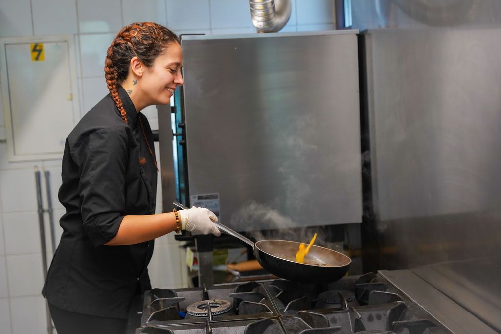 Lo chef prepara del cibo in una cucina in acciaio inossidabile, mescolando il contenuto di una padella sui fornelli.