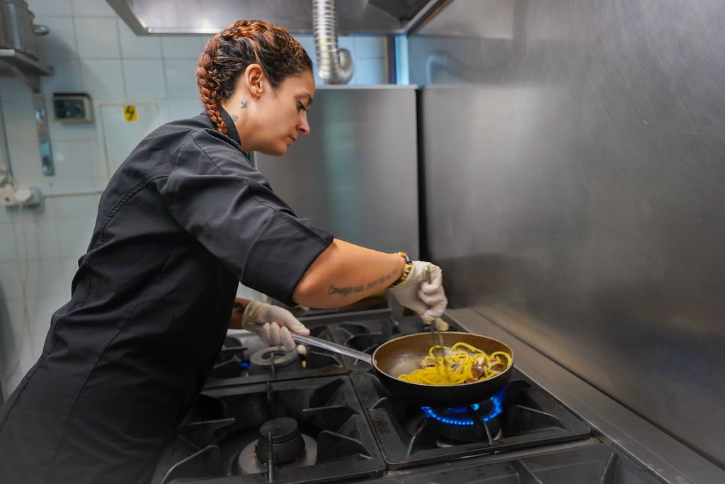 Uno chef mescola il cibo in una padella su una fiamma a gas blu in una cucina professionale.