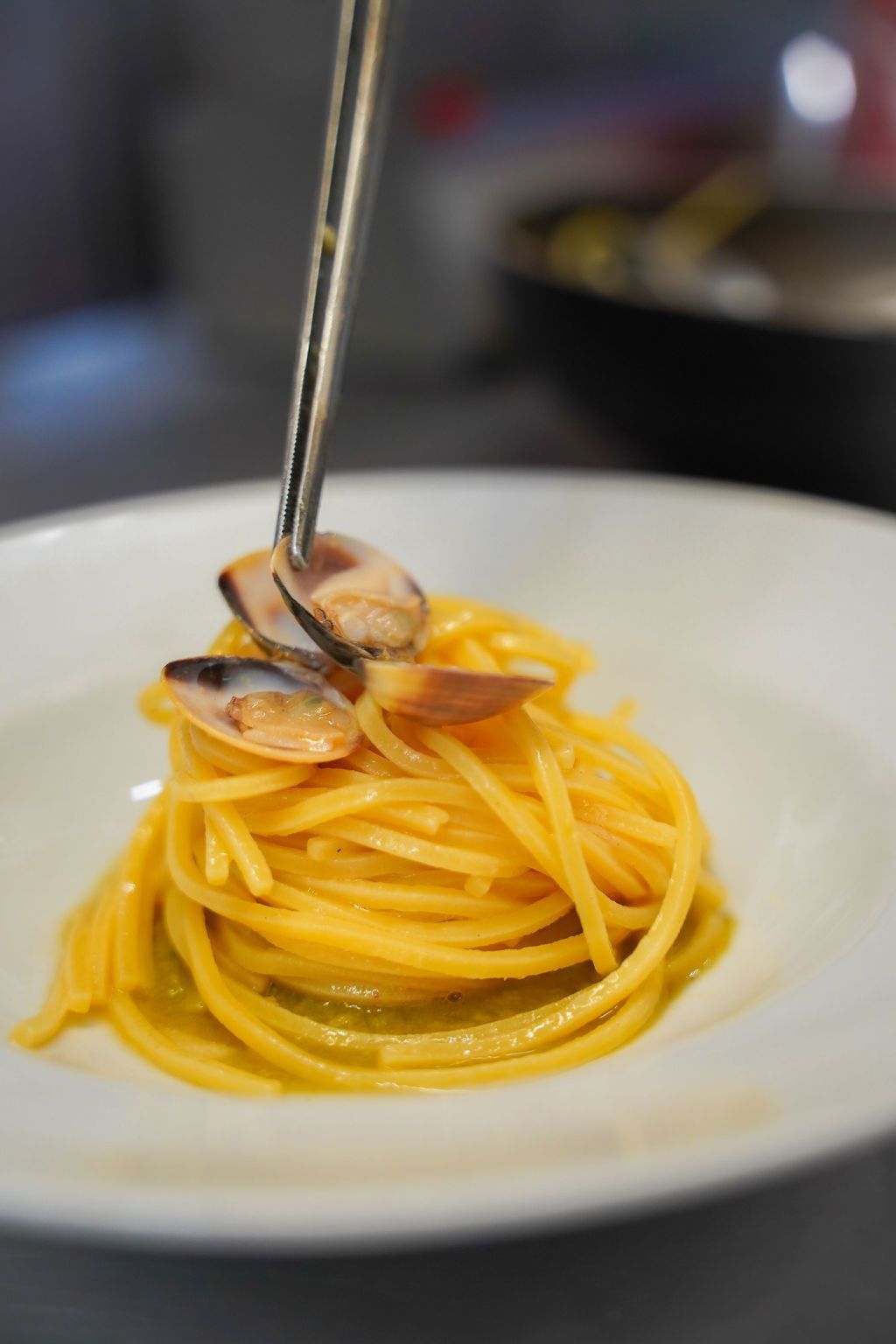 Spaghetti con le vongole su un piatto bianco, da arrotolare con le bacchette o con la forchetta.