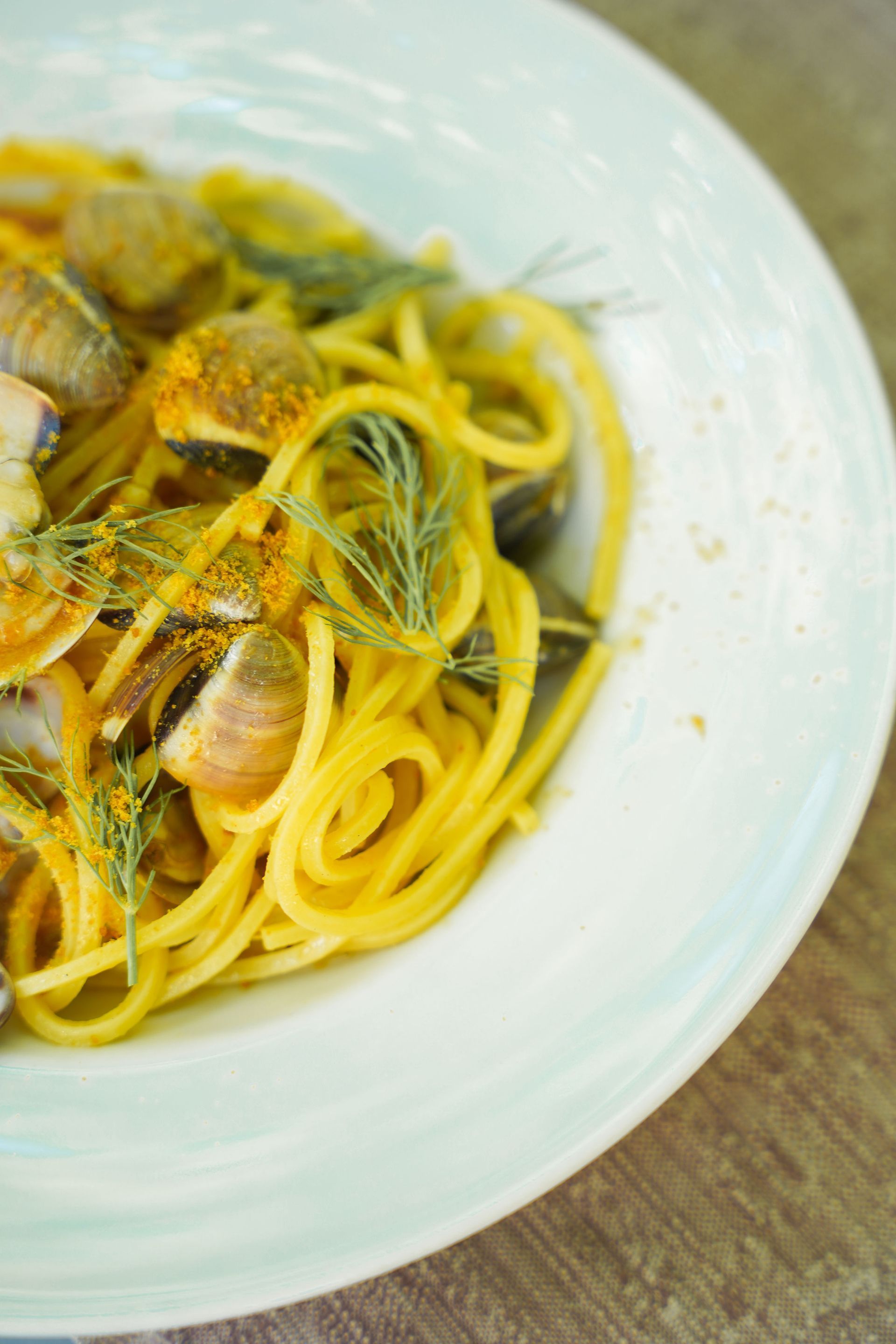 Piatto di pasta ai frutti di mare con cozze e vongole in salsa d'arancia su una tovaglia a quadri.