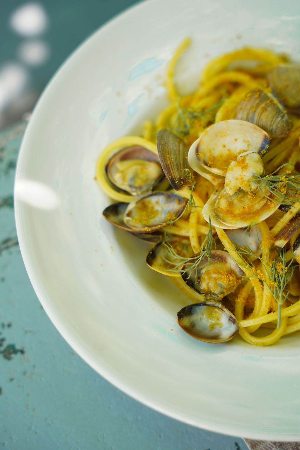 Una ciotola bianca di pasta con vongole e salsa gialla su un tavolo azzurro pallido.