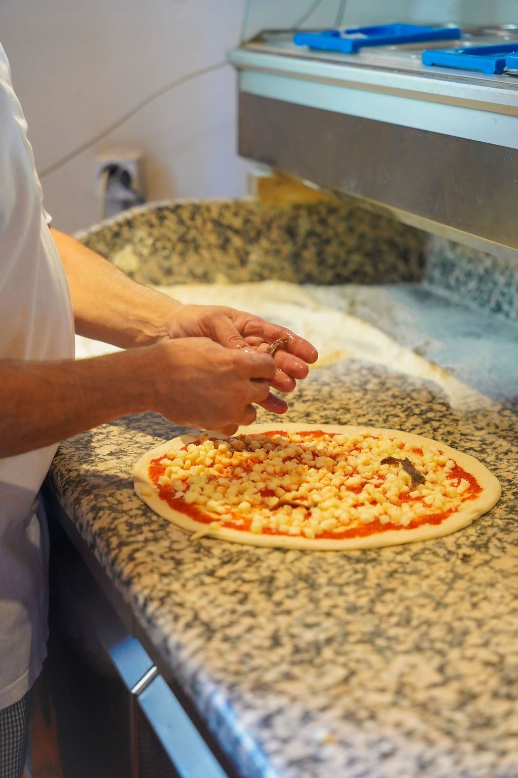 Mani che modellano l'impasto della pizza, condita con formaggio e salsa di pomodoro, su un bancone della cucina.