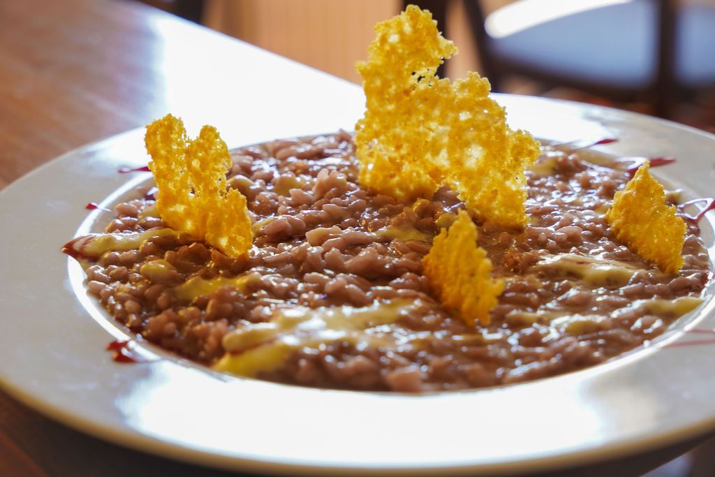 Un piatto bianco di cremoso risotto guarnito con una croccante decorazione dorata, adagiato su un tavolo di legno.